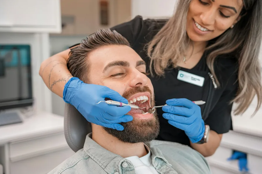 Dentist examining a smiling male patient's teeth during a dental check-up